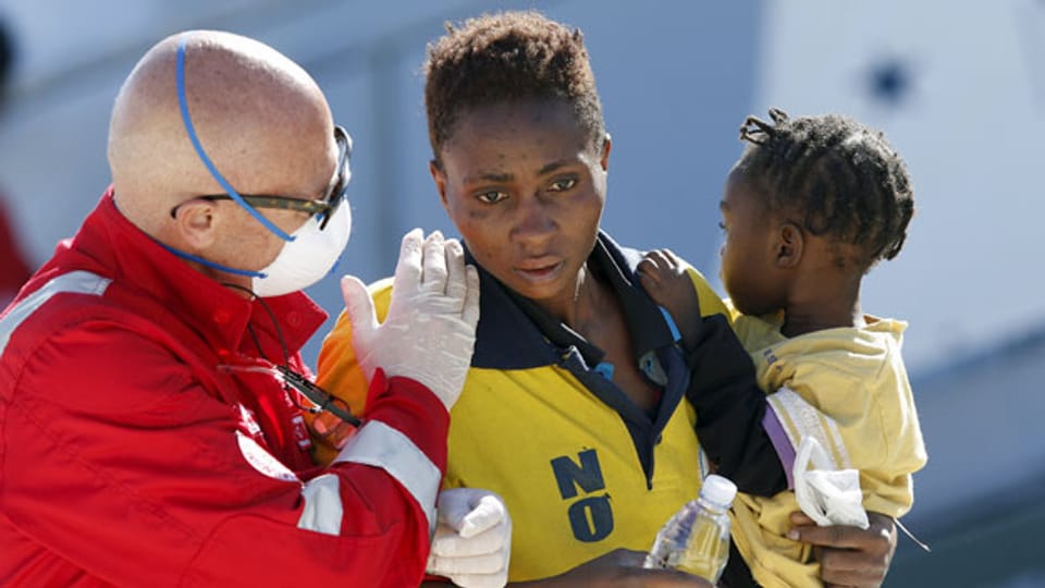 Ein Helfer betreut eine Flüchtlingsfrau und ihr Kind bei der Ankunft in Sizilien.