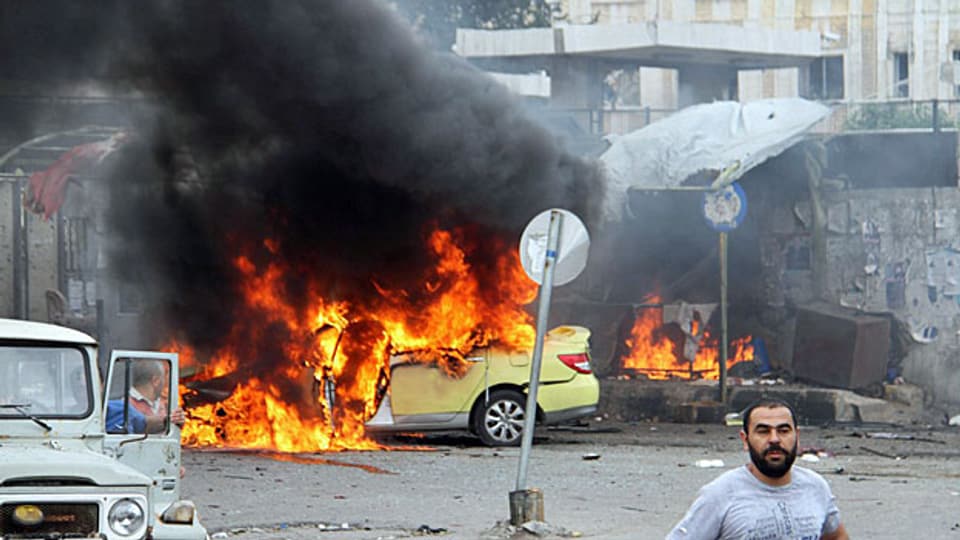 Mindestens 48 Menschen sind laut der syrischen Beobachtungsstelle für Menschenrechte in der syrischen Küstenstadt Tartus umgekommen. Bild: Flammen schiessen aus einem Auto an einer Bushaltestelle in Tartus.