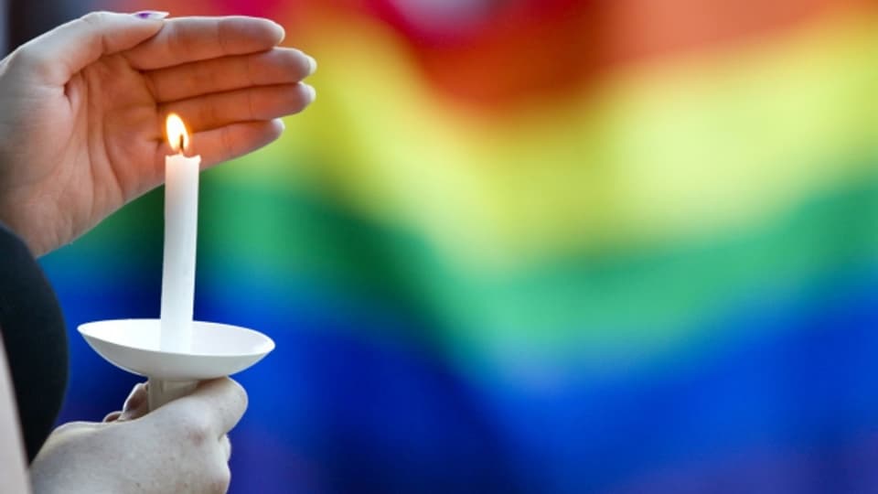 Eine Kerze brennt vor den Regenbogenfarben der Gay-Community.