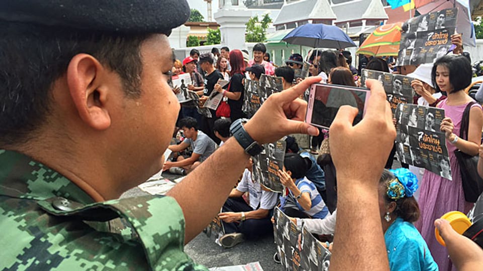«Wir haben das Recht zu protestieren! Wir verstossen gegen kein Gesetz!» Eine kleine Gruppe demonstriert mit Postern vor dem Militärgericht in Bangkok. Ein Polizist fotografiert die Demonstranten, ein anderer fordert sie bald auf, zu schweigen.