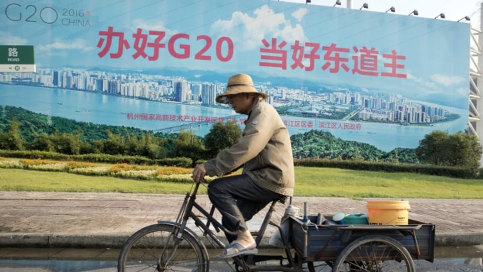Ein Velofahrer vor einem Propaganda-Plakat mit der Aufschrift "G20 gut organisieren, ein guter Gastgeber sein"
