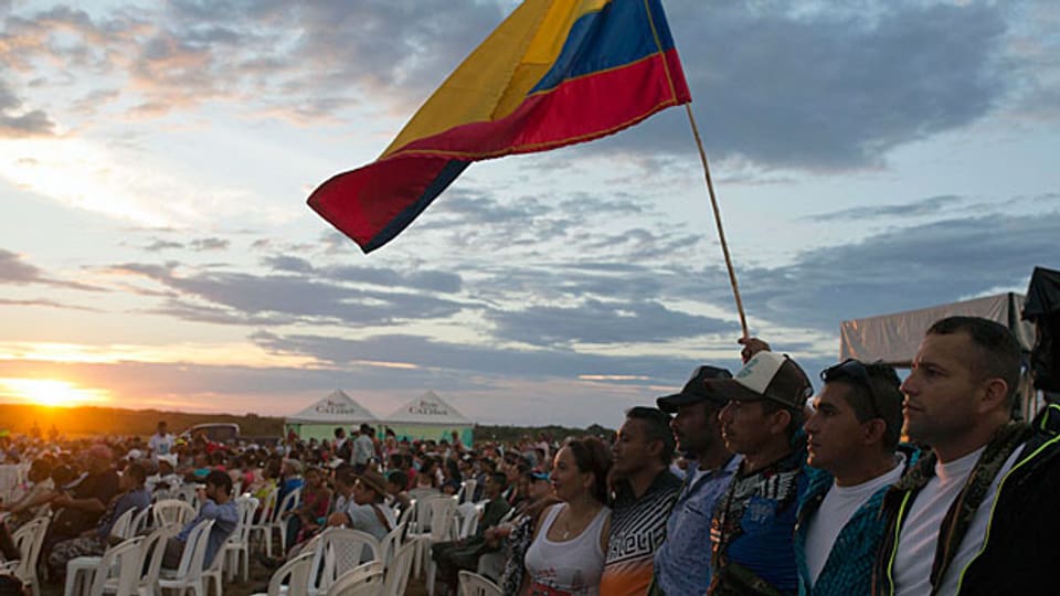 Während einer LIVE-Übertragung der Feier zur Unterzeichnung des Friedensvertrags zwischen Regierung und FARC-Rebellen umarmen sich Männer und Frauen im Süden des Landes und schwenken eine kolumbianische Flagge.