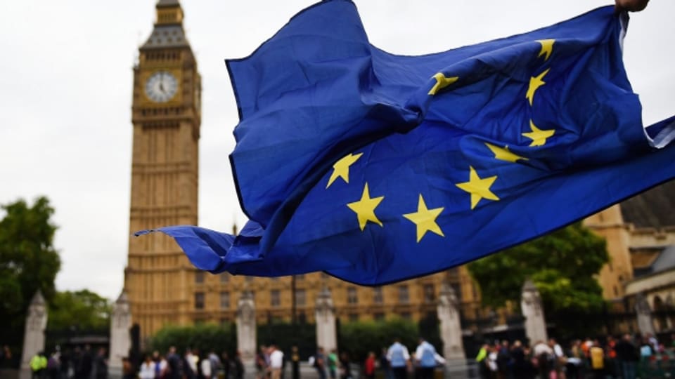 Auf dem Bild ist eine EU-Flagge zu sehen, im Hintergrund das britische Parlament in London. Wegen des Brexit zieht es vermehrt Spitzenleute von britischen Universitäten zurück aufs europäische Festland.