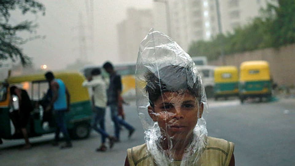 In einer Strasse von Delhi herrscht dichter Smog; ein kleiner Junge hat sich als Schutz vor der schlechten Luft einen Plasticsack über den Kopf gezogen.