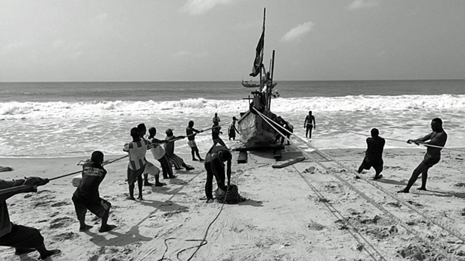 Fischer ziehen in Totope an der westafrikanischen Küste in Ghana ein traditionelles Fischerboot auf den Strand.