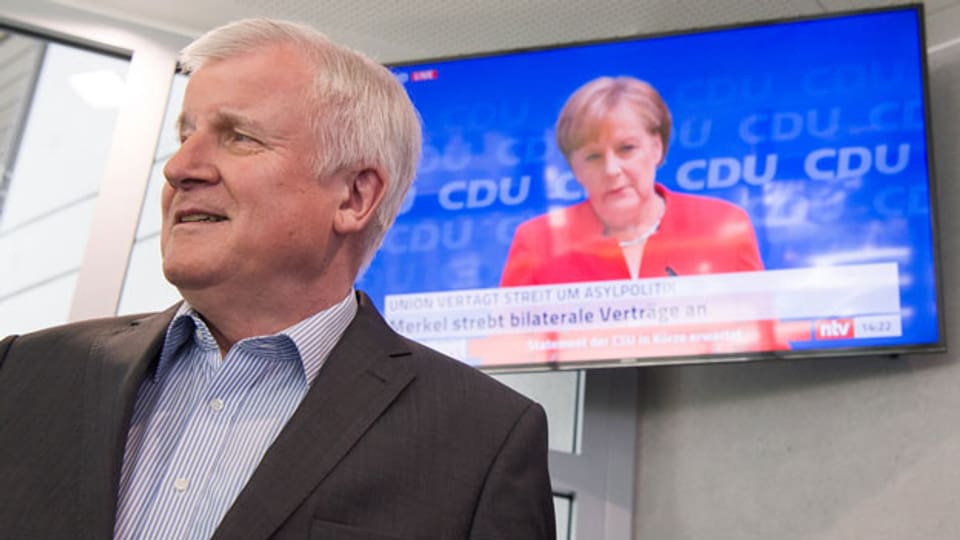 Horst Seehofer, CSU-Vorsitzender, geht an einem Fernseher vorbei, auf dem die Pressekonferenz von Bundeskanzlerin Angela Merkel (CDU) übertragen wird.