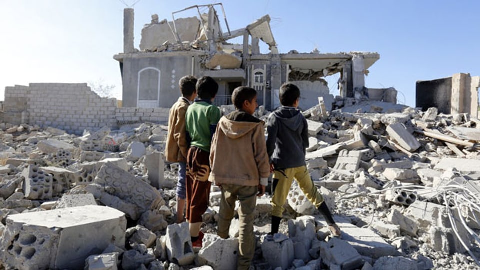 Kinder in Jemen stehen vor den Trümmern einiger Häuser.
