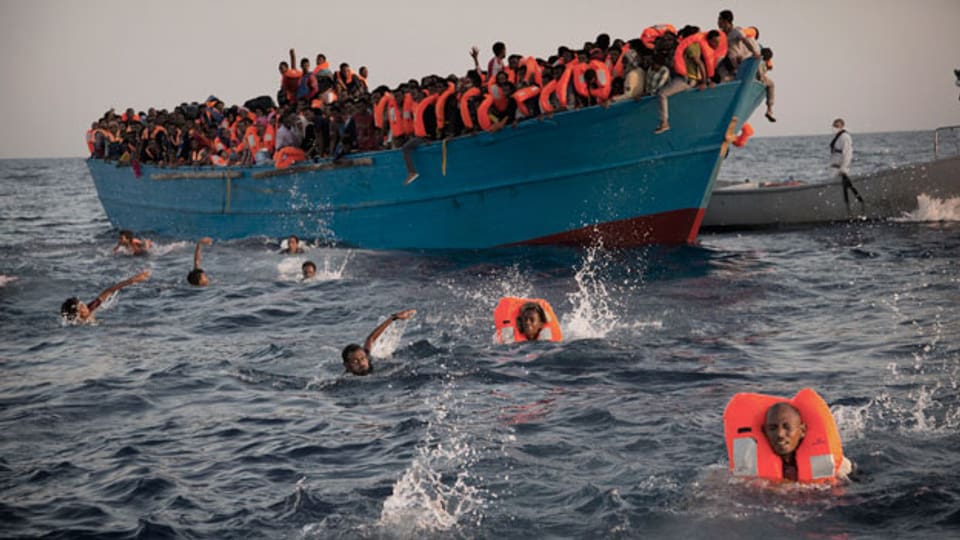 Migranten springen von einem überfüllten Holzboot ins Wasser vor Libyen.