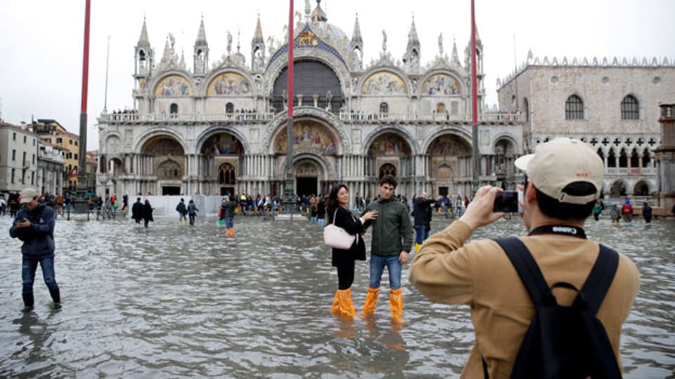 Touristen posieren für Fotos auf dem überfluteten Markusplatz in Venedig.