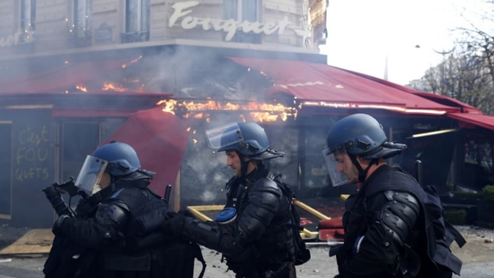Polizisten stehen vor einem zerstörten Lokal in der Pariser Innenstadt (Proteste vom vergangenen Samstag 16.3.).