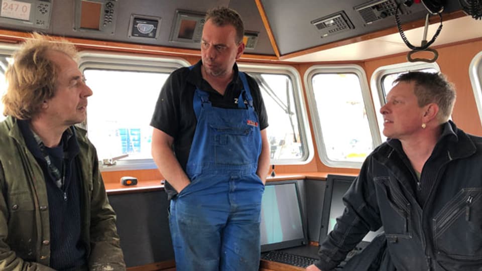 Der 38jährige Robin Bouma (Mitte) ist Crevettenfischer. Von Sonntagnacht bis Freitagmorgen ist er mit seiner Crew auf der Nordsee unterwegs. Im Steuerhaus, wo es angenehm warm ist, tauscht der Kutter-Besitzer die letzten Neuigkeiten mit zwei Kollegen aus.