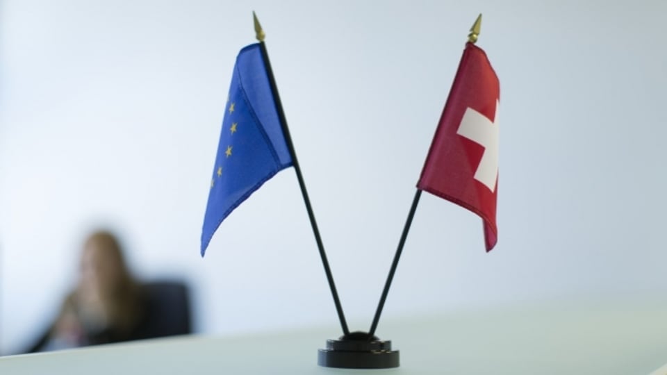 Eine Schweizer Flagge und die der EU, fotografiert auf einem Bürotisch.