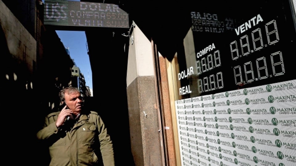 Passant in Buenos Aires, Argentinien, vor einen Bildschirm, der den Wert der Fremdwährungen in Bezug auf den argentinischen Peso unter Führung des Dollars anzeigt.