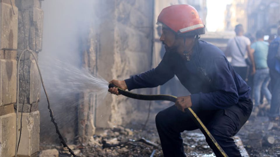 Ein Feuerwehrmann spritzt Wasser an der Stelle einer Autobombenexplosion vor einer Kirche in Qamischli, Afghanistan Syrien, 11. Juli 2019.