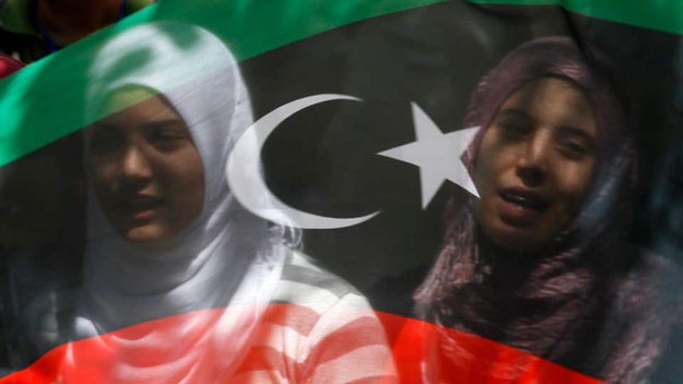 Lybien-Fahne, auf welcher sich Gesichter von zwei Frauen spiegeln.