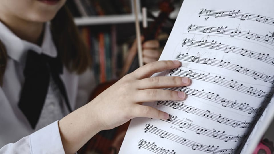 Ein Mädchen musiziert ab einem Musiknotenblatt.