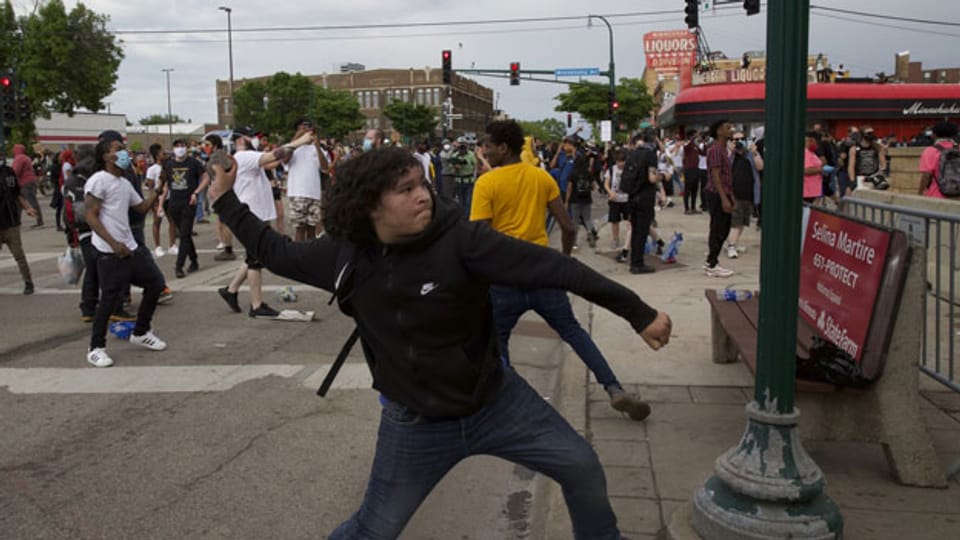 Ein Mann wirft einen Stein gegen die Polizei von Minneapolis.