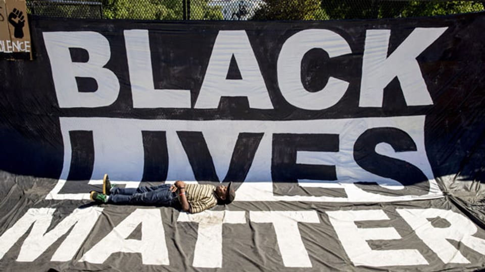 Ein schwarzer Mann liegt auf einer Black Lives Matter-Fahne in den USA.