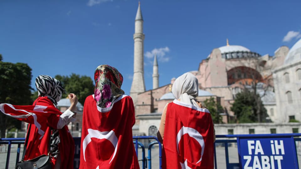 Menschen, umhüllt mit einer türkischen Flagge, freuen sich,  dass das 1500 Jahre alte Unesco-Weltkulturerbe Hagia Sophia in Istanbul, Türkei, in eine Moschee umgewandelt werden kann.