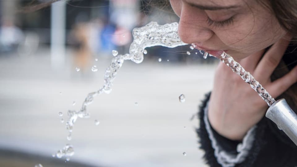 Eine Frau trinkt Trinkwasser von einem Brunnen.