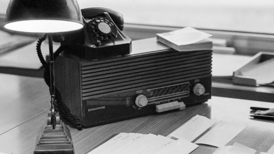 Eine Tischlampe, ein Telefon, ein Radioempfaenger der Marke Biennophon und Nachrichtenmeldungen auf einem Pult in der Radioredaktion der Schweizerischen Depeschenagentur SDA in Bern, aufgenommen am 13. Januar 1969.