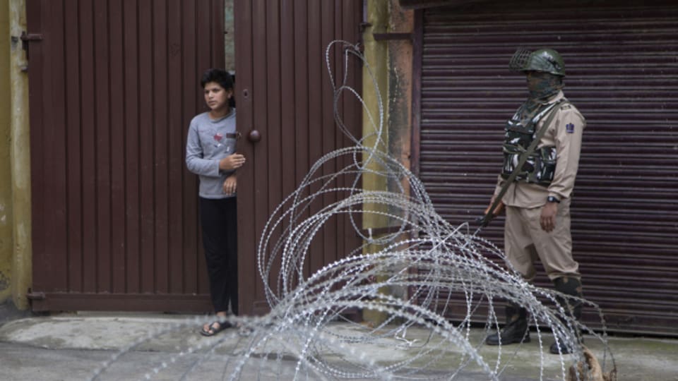 Ein kaschmirischer Junge schaut aus seinem Haus, als ein indischer paramilitärischer Soldat in Srinagar, dem von Indien kontrollierten Kaschmir, an einem Kontrollpunkt Wache hält, im August 2020.
