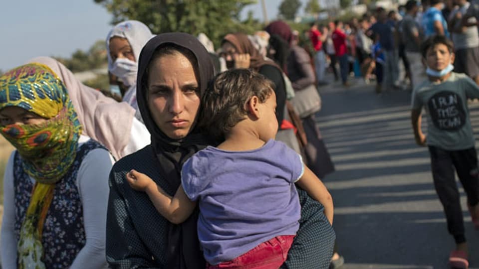 Eine Frau hält ein Baby im Arm, während sie zusammen mit anderen Migranten auf der nordöstlichen Insel Lesbos, in einer Schlange auf die Lebensmittelverteilung wartet. 12. September 2020.