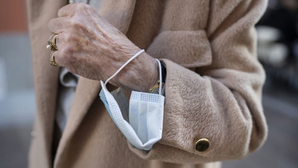 Eine ältere Frau trägt eine Hygienemaske um das Handgelenk.