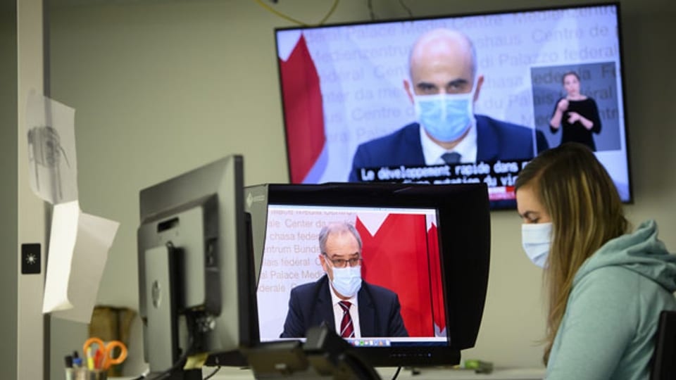 Eine Journalistin mit Gesichtsmaske beobachtet Gesundheitsminister Alain Berset (oben) und den Bundespräsidenten Guy Parmelin (links), die neue Massnahmen gegen das Coronavirus ankündigen.