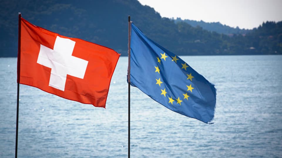 Die Schweizer Nationalflagge und die Europaflagge flattern nebeneinander am Lago Maggiore.