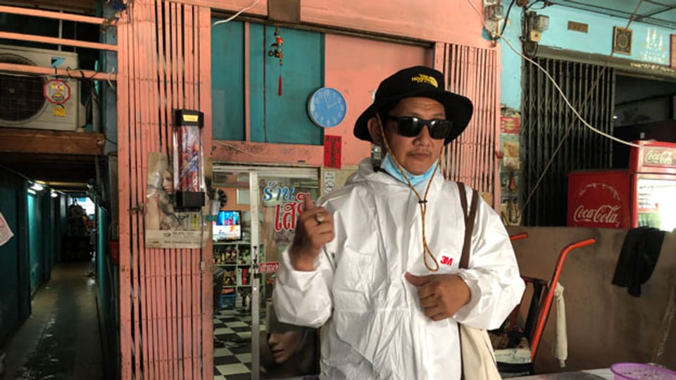 Pipat Kornmek ist eingehüllt in einen weissen Plastikanzug. Geschützt mit Sonnenbrille, Maske und Hut fährt er seit Tagen mit seinem Motorrad durch das Armenviertel und verteilt Pakete an die Kranken.
