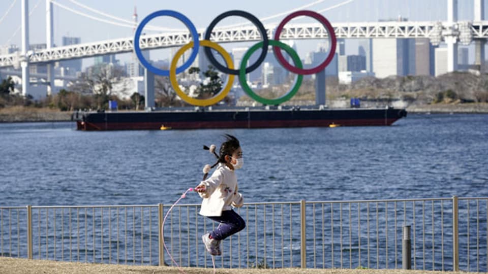 Ein Mädchen springt mit einem Seil vor einem riesigen Denkmal der Olympischen Ringe im Odaiba Marine Park in Tokio, Japan, am 11. Februar 2021.