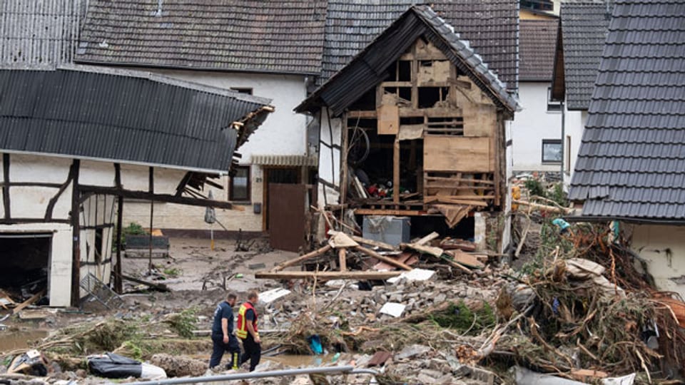 Rheinland-Pfalz, Schuld: Zwei Feuerwehrleute gehen in dem Dorf im Kreis Ahrweiler nach dem Unwetter mit Hochwasser durch den Schutt. Mindestens sechs Häuser wurden durch die Fluten zerstört.