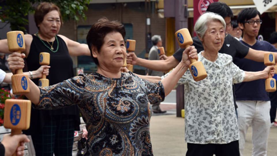 Ältere Menschen trainieren mit hölzernen Hanteln auf dem Gelände eines Tempels in Tokio.