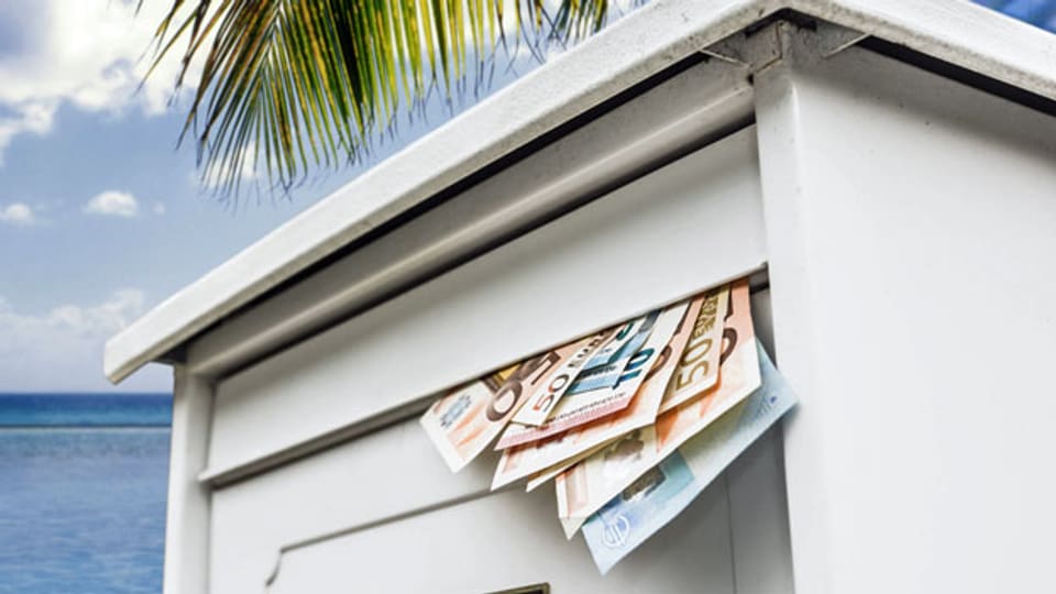 Symbolbild: Geldscheine ragen aus einem Briefkasten auf einer tropischen Insel.
