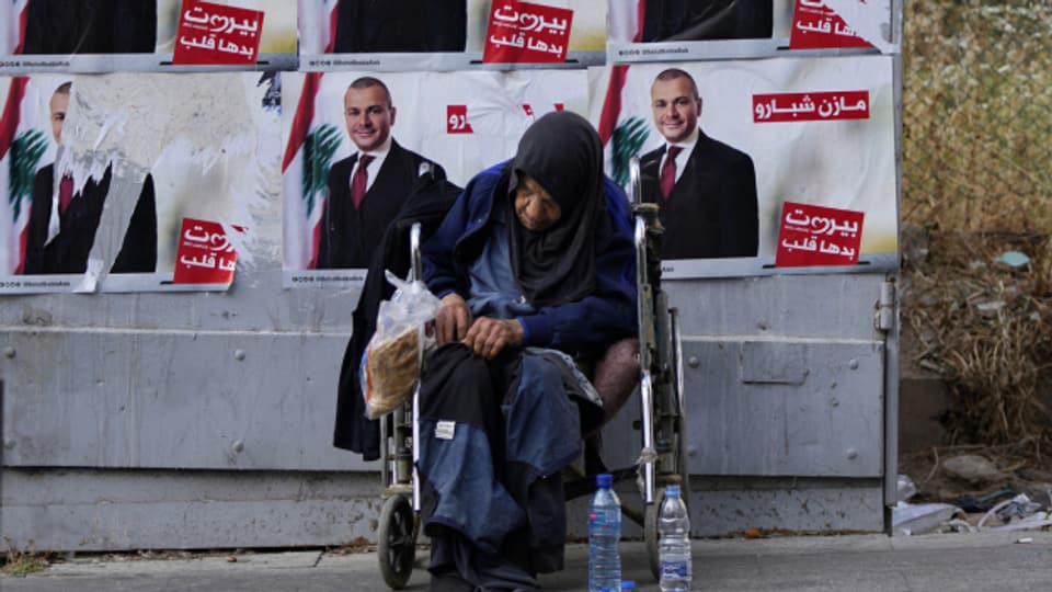 Eine ältere, obdachlose Frau sitzt im Rollstuhl vor Wahlkampfplakaten in Beirut im Mai 2022.