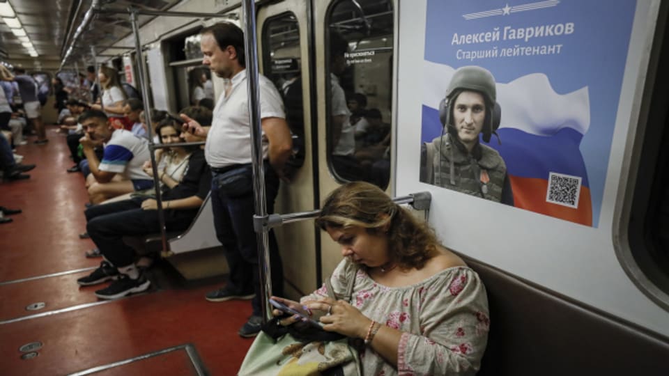 Eine Frau sitzt in der U-Bahn vor einem Poster, das einen russischen Soldat zeigt