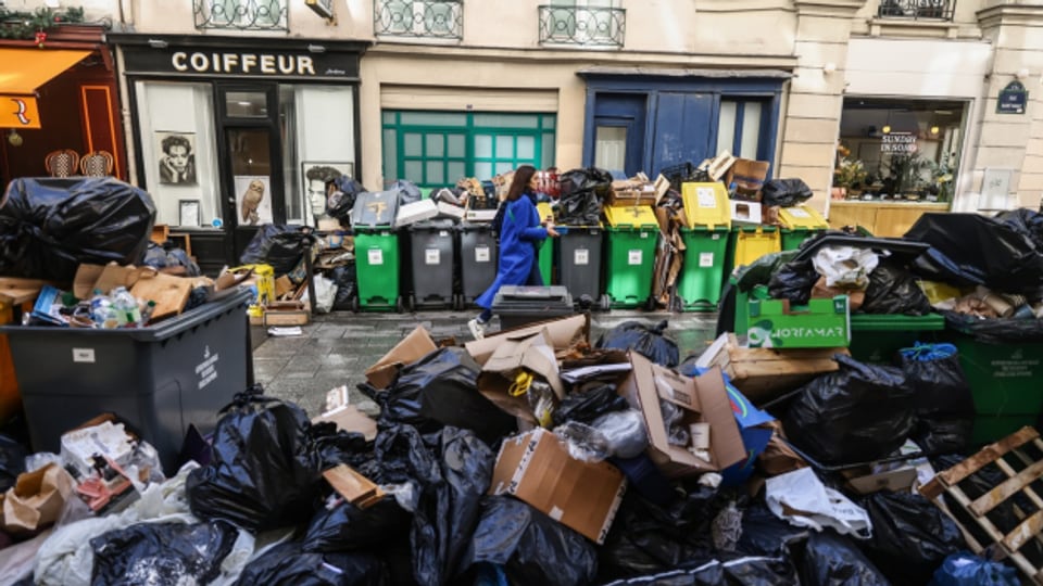 Eine Passantin läuft in Paris an überfüllten Mülltonnen und unzähligen Abfallsäcken vorbei.