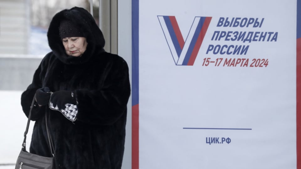 Eine Frau wartet an einer Bushaltestelle in Moskau neben einem Wahlkampfplakat mit der Aufschrift "Die Wahlen des Präsidenten von Russland. 15.-17. März 2024".