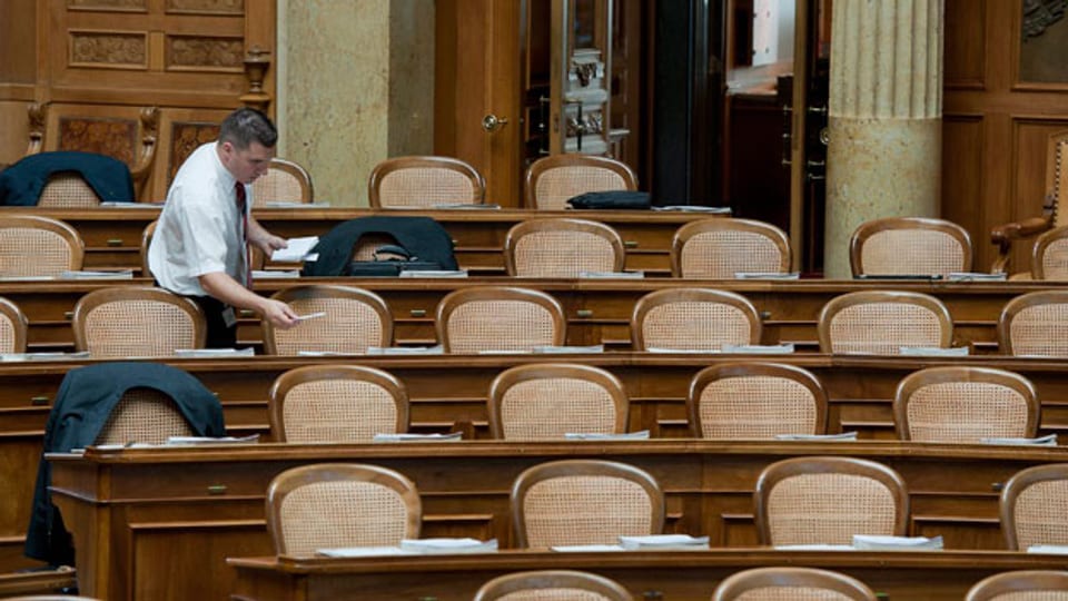 An zwei von drei Pulten im Nationalratssaal sitzen Männer.