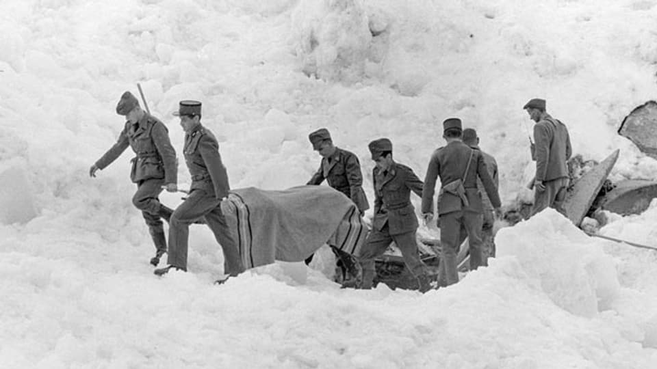 Soldaten und ein Polizist bergen ein Opfer auf dem zerstörten Barackenlager der Baustelle des Mattmarkstausees nach dem Niedergang einer Eislawine am 30. August 1965, der 88 Menschenleben forderte.