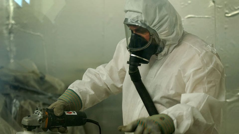 Ein Arbeiter mit Atemschutz und Schutzanzug befreit Rohre und Leitungen von Asbestrückständen.