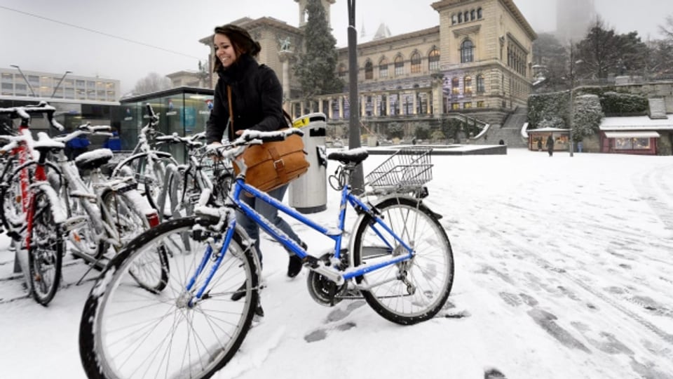 Eine Frau sösst ihr Fahrrad in Lausanne über den Place de la Riponne.