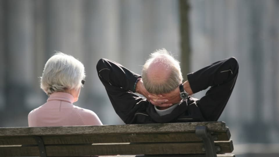 Ein Rentnerpaar sitzt auf einer Bank und sonnt sich.