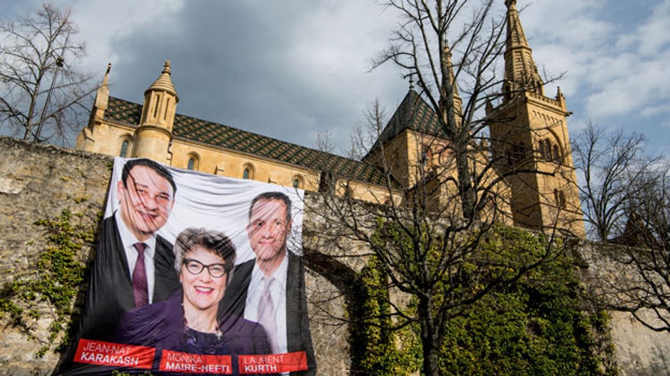 Ein Wahlplakat in Neuchâtel mit den drei Kandidaten  Jean-Nat Karakash, Monika Maire-Hefti und Laurent Kurth.