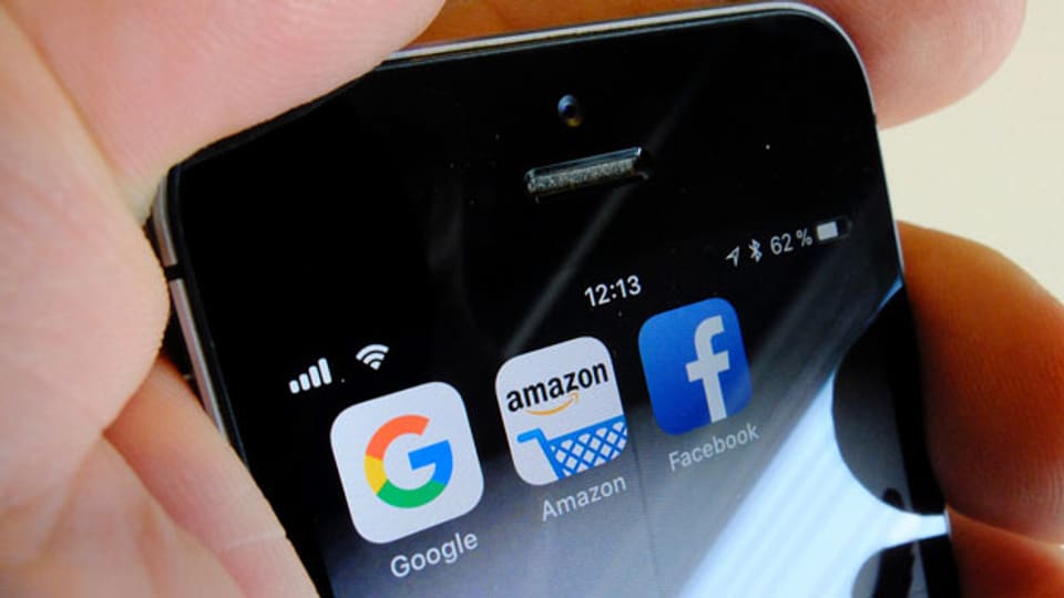 Die Logos der US-Internetkonzerne Google, Amazon und Facebook sind auf dem Display eines iPhone zu sehen.