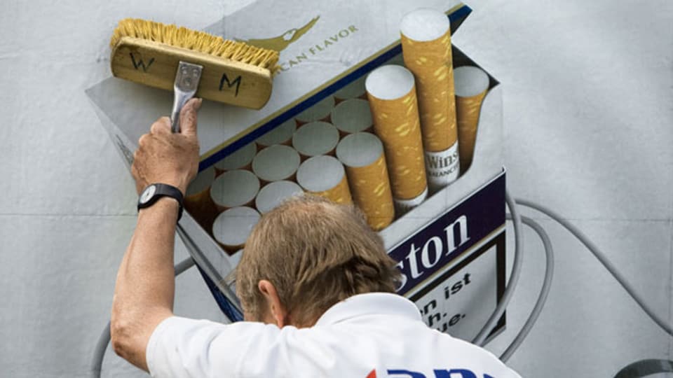 Symbolbild. Ein Plakat mit Tabakwerbung wird aufgehängt.