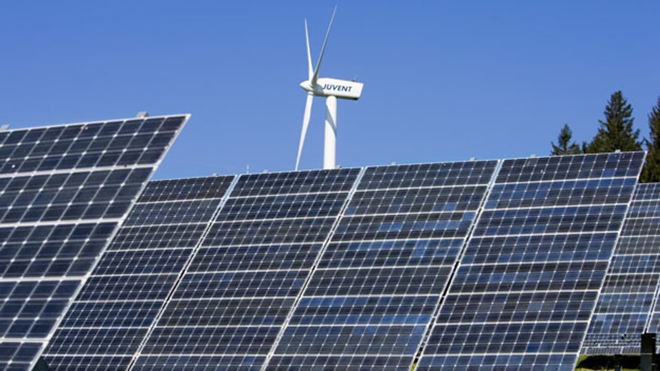 Symbolbild. Solarzellen eines Fotovoltaik-Sonnenkraftwerks und dahinter eine Windturbine.