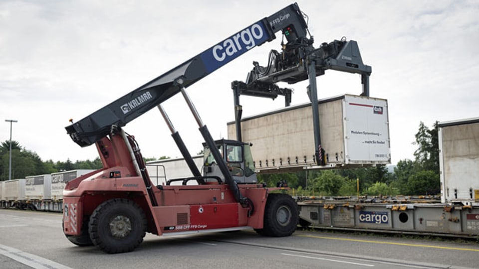 Mit einem fahrbaren Kran werden Container von LKWs auf die Schiene verladen.