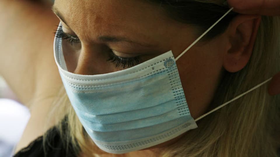 Symbolbild. Eine Frau schützt sich mit einer Mundschutz-Maske.
